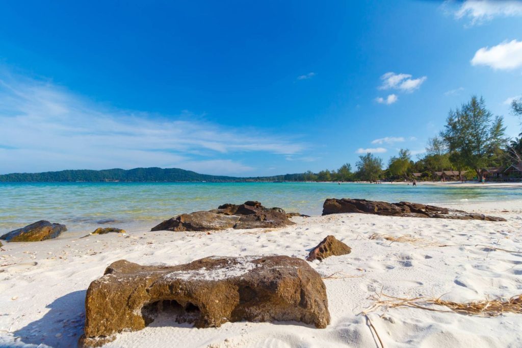 Pristine white sand beach with turquoise waters, rocky shoreline, and clear blue sky, showcasing relaxing coastal scenery as one of the top Things to Do in Cambodia.