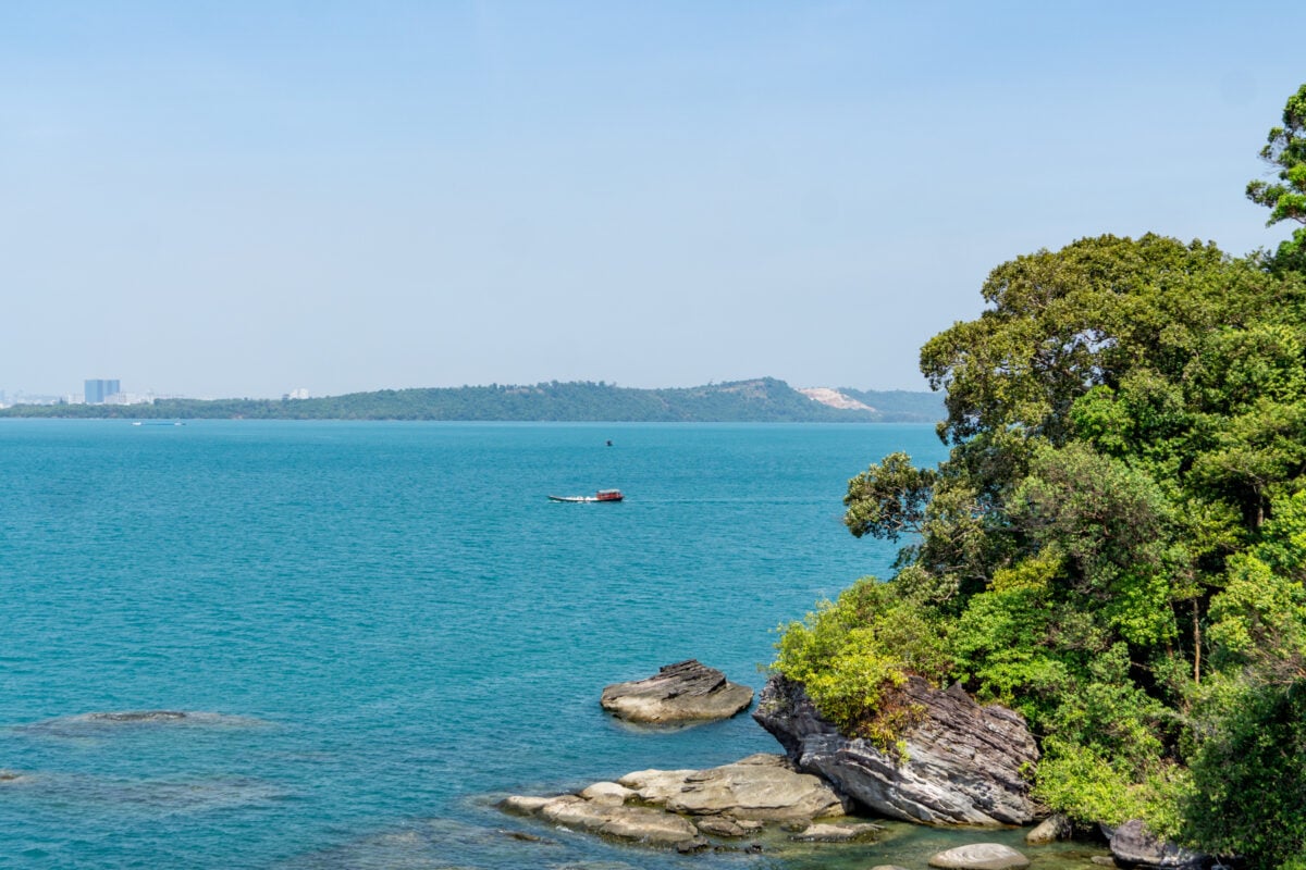 Scenic coastal viewpoint with turquoise sea, rocky shoreline, and lush green forest, highlighting island exploration and nature escapes as popular Things to Do in Cambodia.