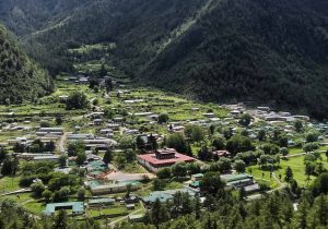 Best Things to Do in Bhutan featuring a scenic aerial view of a peaceful valley village surrounded by lush green mountains, traditional houses, and a central monastery set in pristine nature.