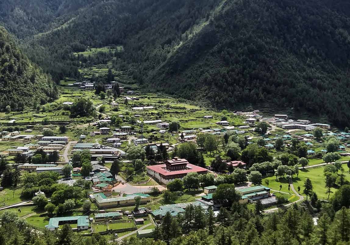 Best Things to Do in Bhutan featuring a scenic aerial view of a peaceful valley village surrounded by lush green mountains, traditional houses, and a central monastery set in pristine nature.