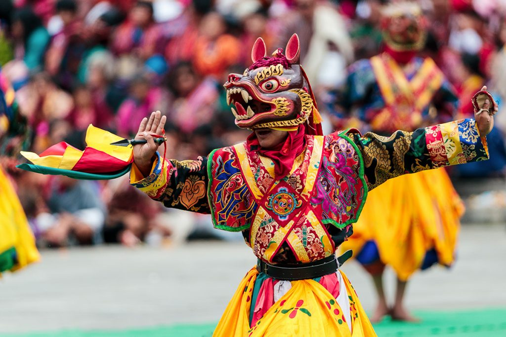 Best Things to Do in Bhutan showcasing a vibrant traditional festival dancer wearing a colorful costume and ornate mask, performing in front of a lively crowd during a cultural celebration.