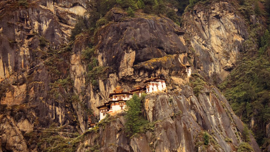 Best Things to Do in Bhutan featuring the iconic Tiger’s Nest Monastery perched dramatically on a steep cliff, surrounded by rugged mountains, pine forests, and prayer flags.